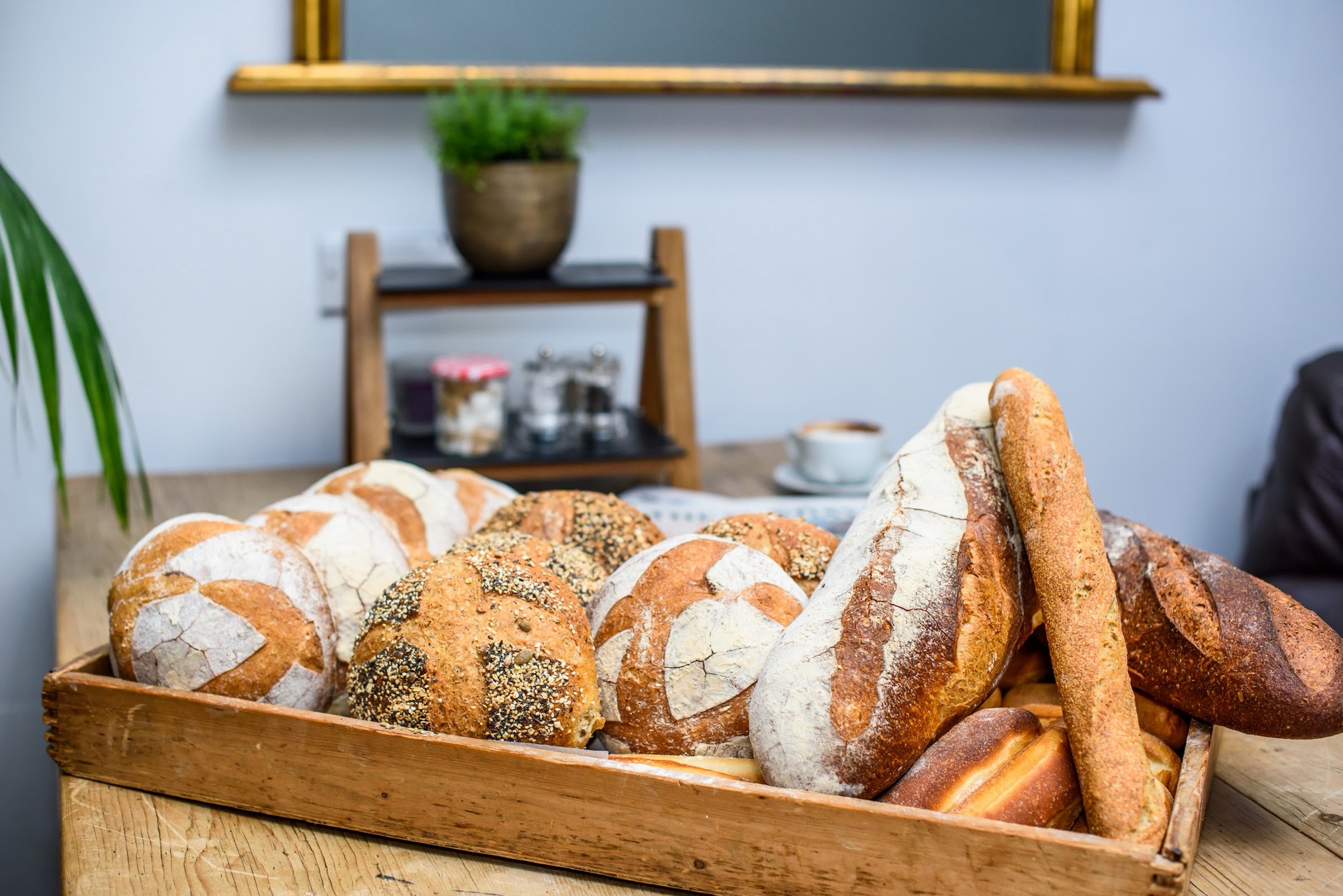 A wooden crate of freshly baked sourdough loaves, seeded rolls and baguettes on the table at La Bakerie, Wanstead