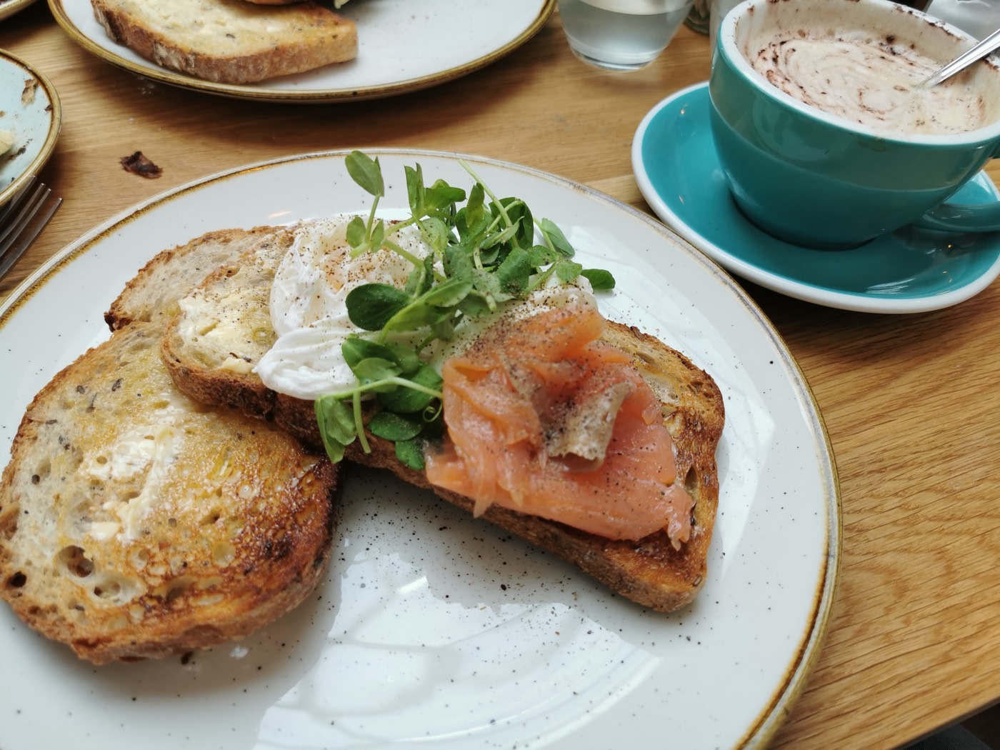 Toasted sourdough topped with smoked salmon, poached egg and pea shoots, with a hot chocolate, at La Bakerie